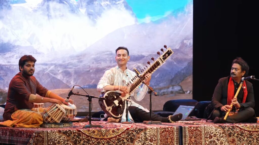 Rishab Rikhiram Sharma playing sitar for mental health in a calm, candlelit setup with audience seated on mats